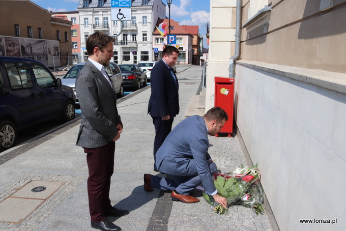 Symboliczne kwiaty przed tablicą składa prezydent Łomży Mariusz Chrzanowski